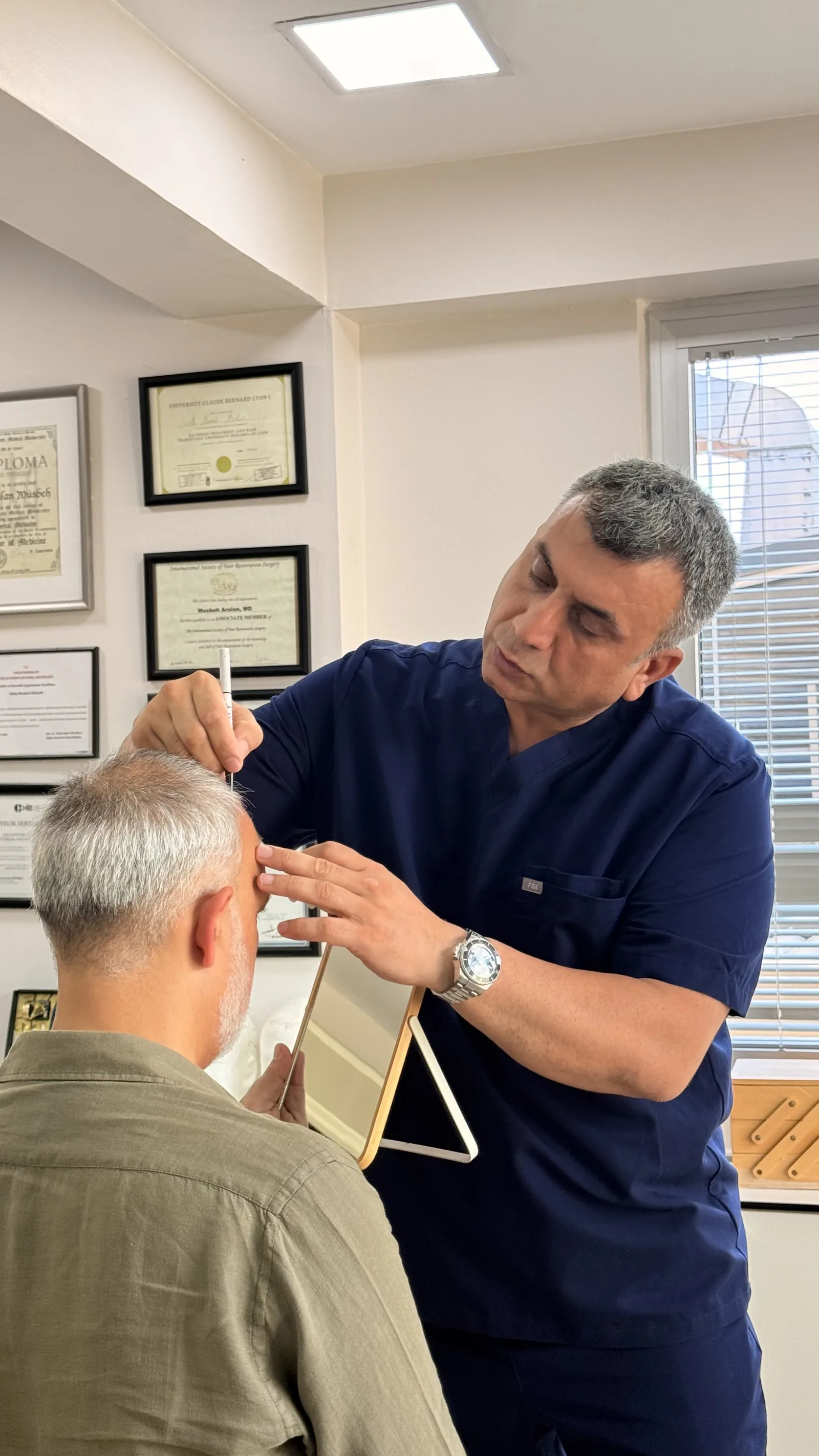 Dr. Arslan Musbeh marking a patient's hairline and donor area by hand during a pre-op consultation