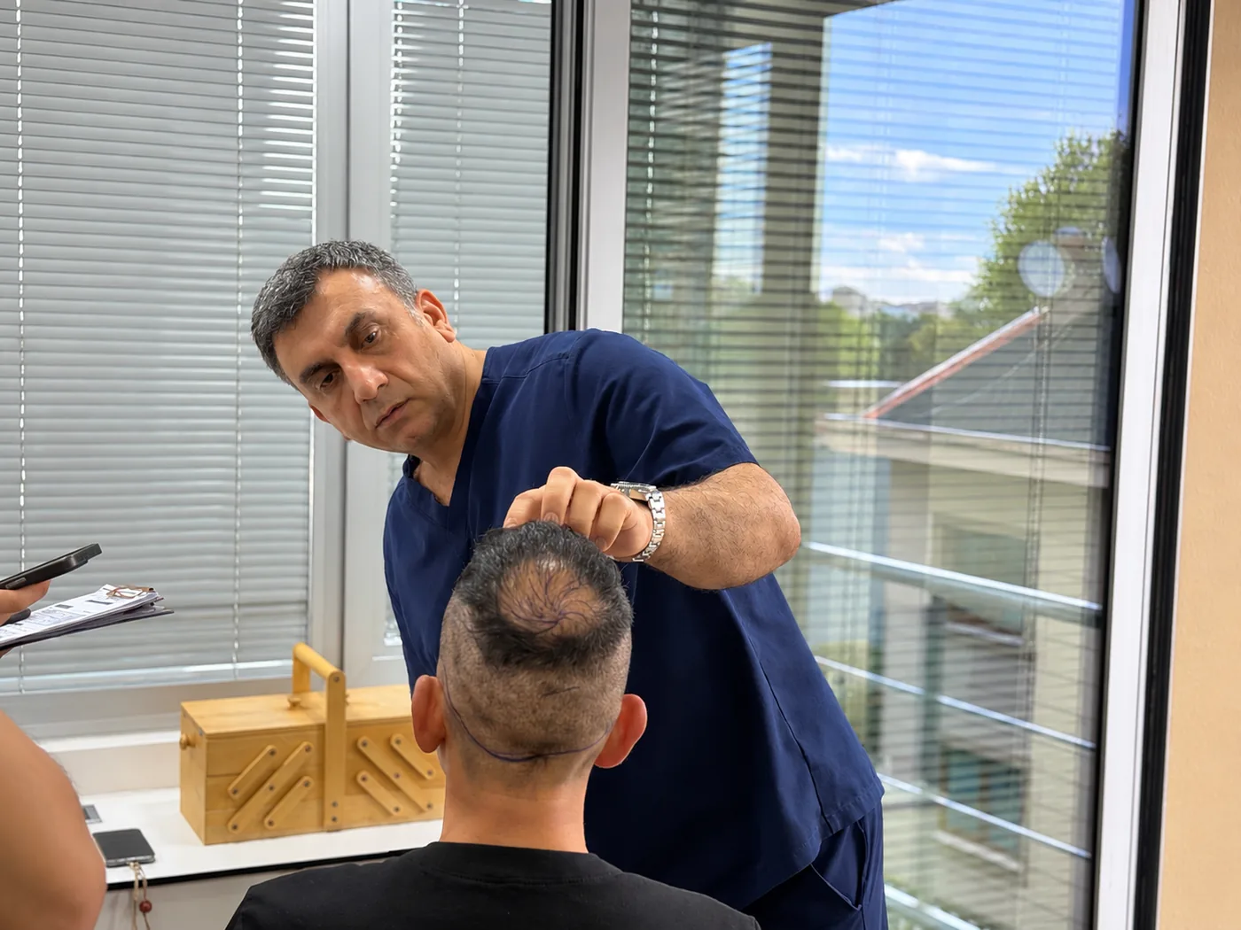 Dr. Arslan Musbeh personally examining a patient's hairline and donor area before treatment planning