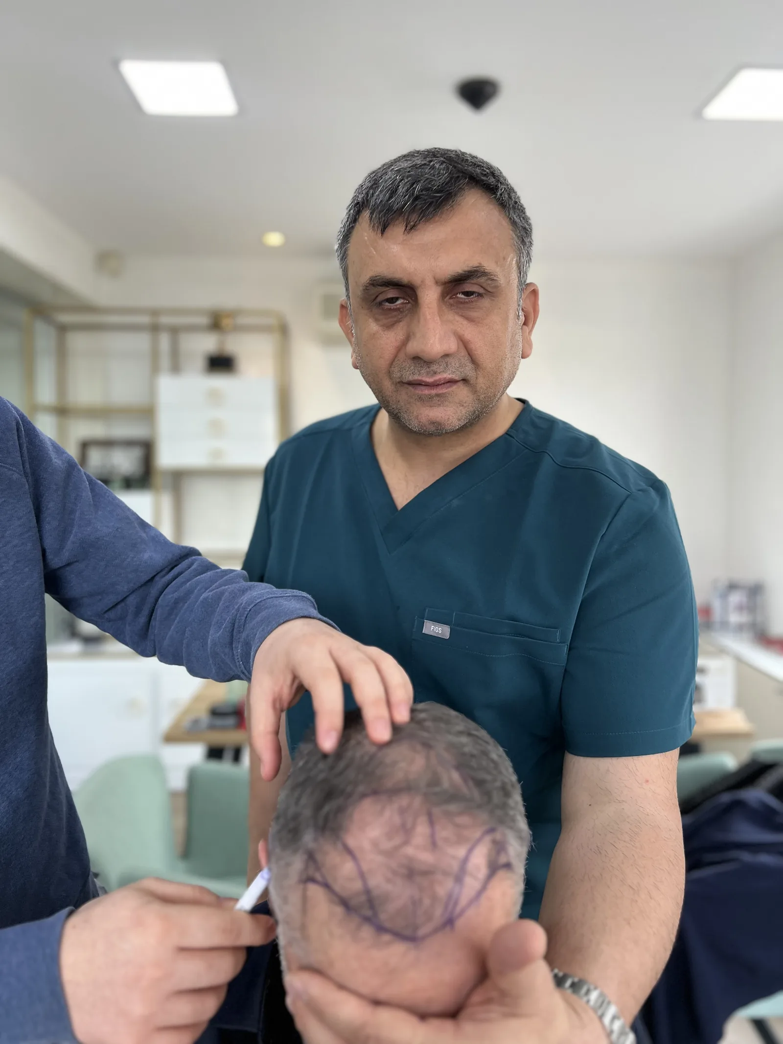 Dr. Arslan Musbeh personally examining a patient's marked hairline during an in-person consultation at Hairmedico