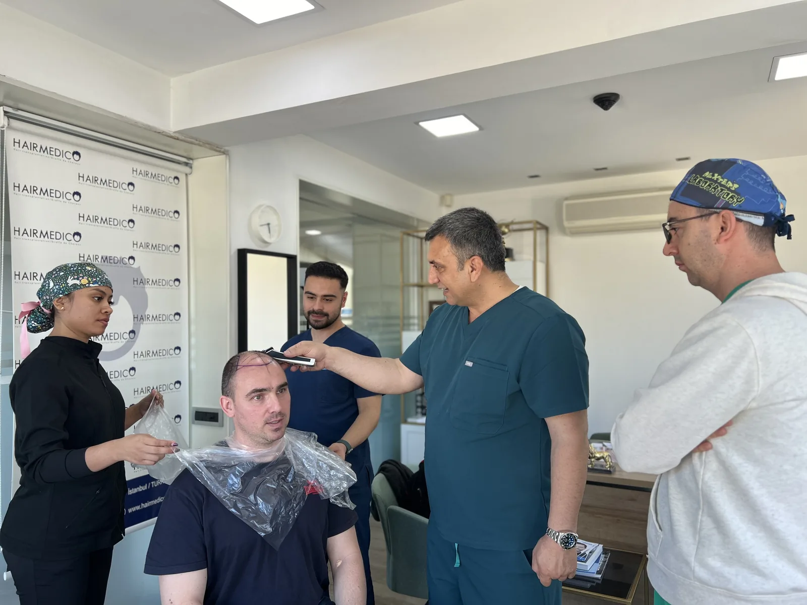 Dr. Arslan Musbeh clipping a patient's hair before surgery while the Hairmedico team prepares the recipient area