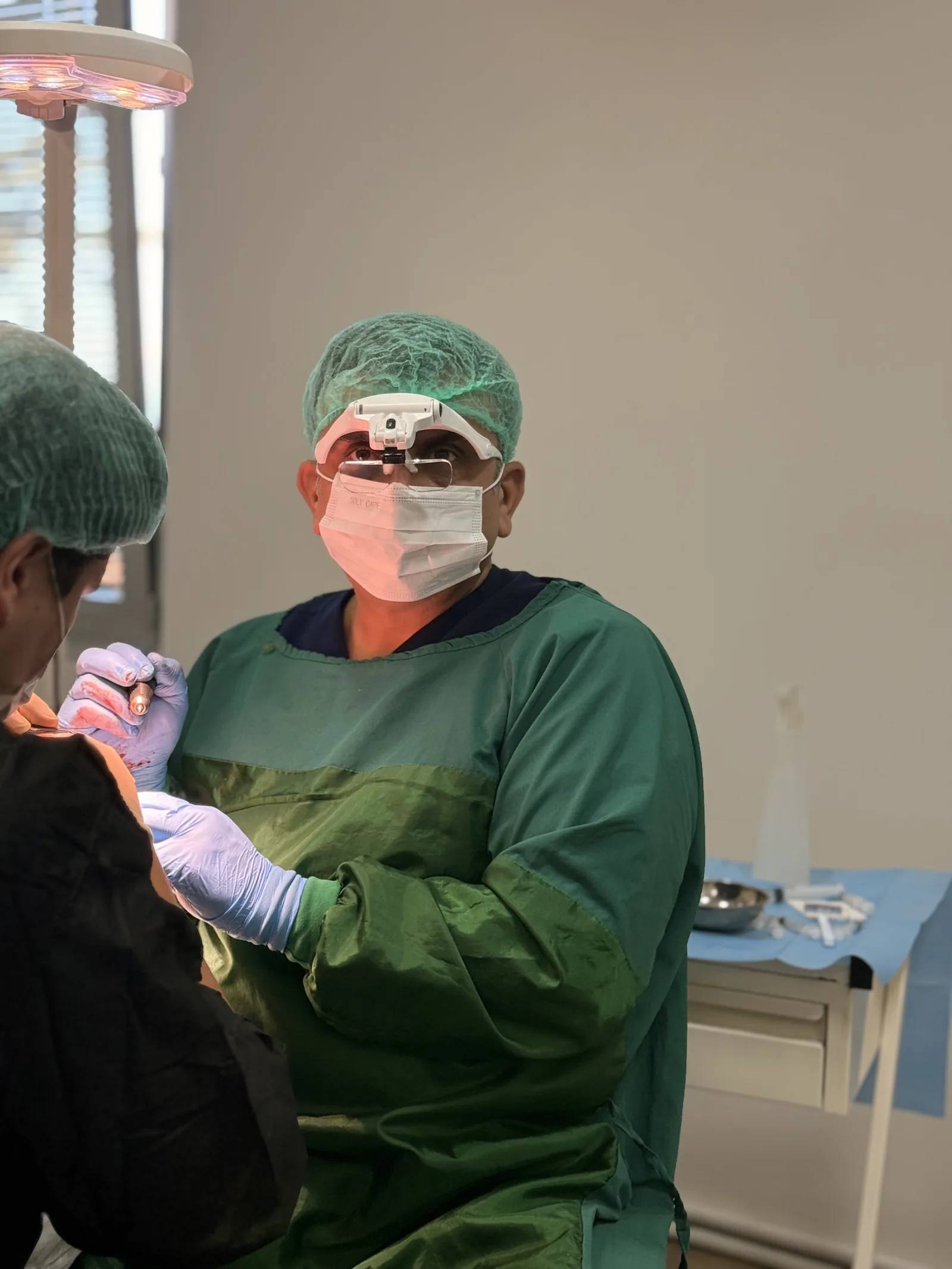 Dr. Arslan Musbeh in surgical loupes and mask performing a follicle extraction under the operating light at Hairmedico