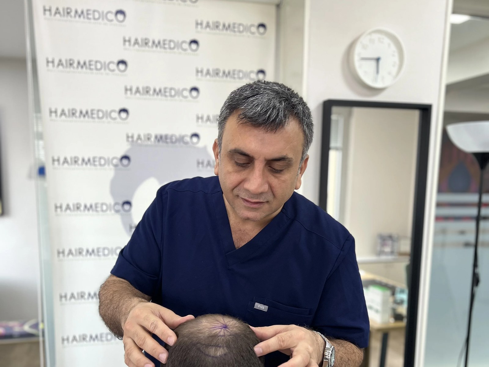 Dr Arslan Musbeh examinant le cuir chevelu d'un patient en consultation