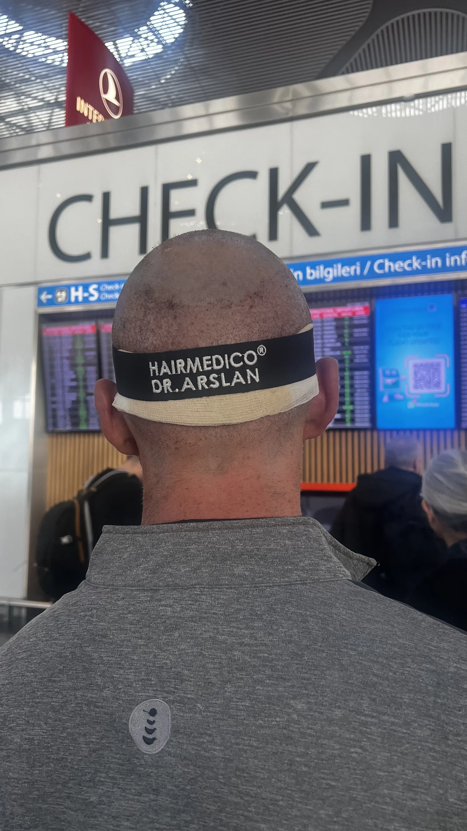 Hairmedico patient wearing the clinic's branded post-procedure headband while checking in for his flight home from Istanbul