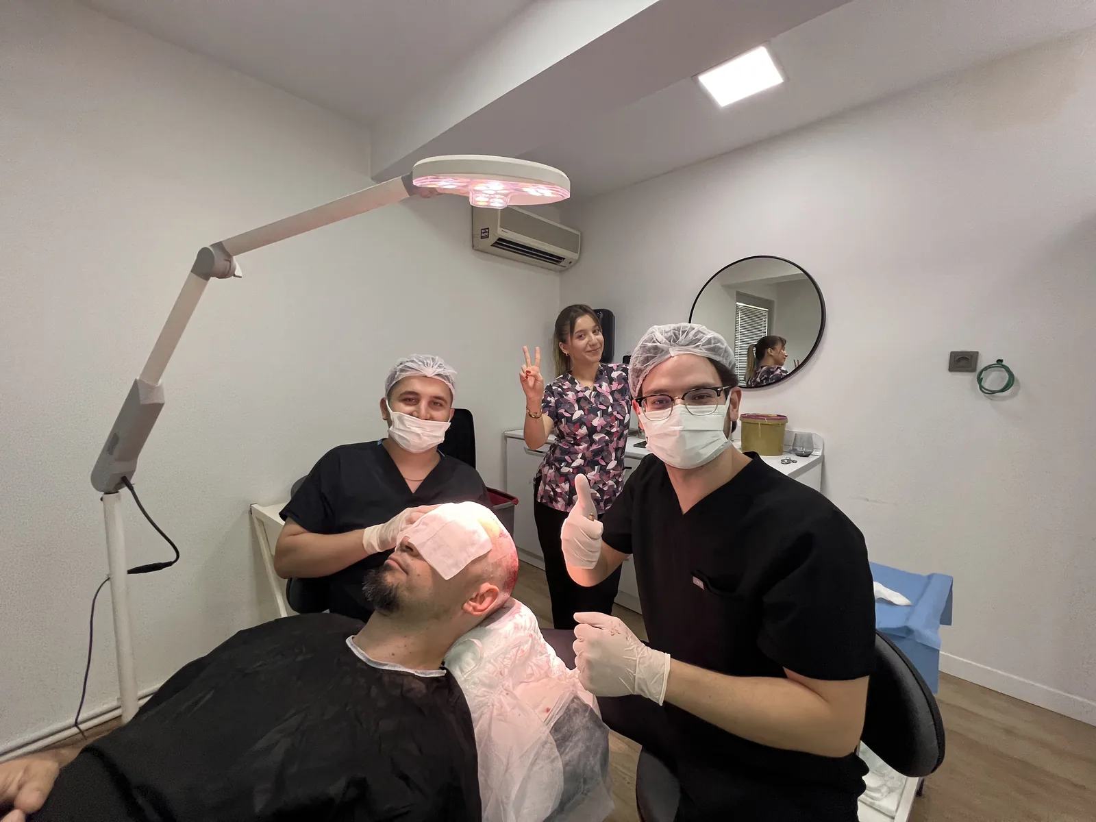 Dr. Arslan's surgical team with a patient immediately after graft placement, scalp protected under the clinic's healing lamp
